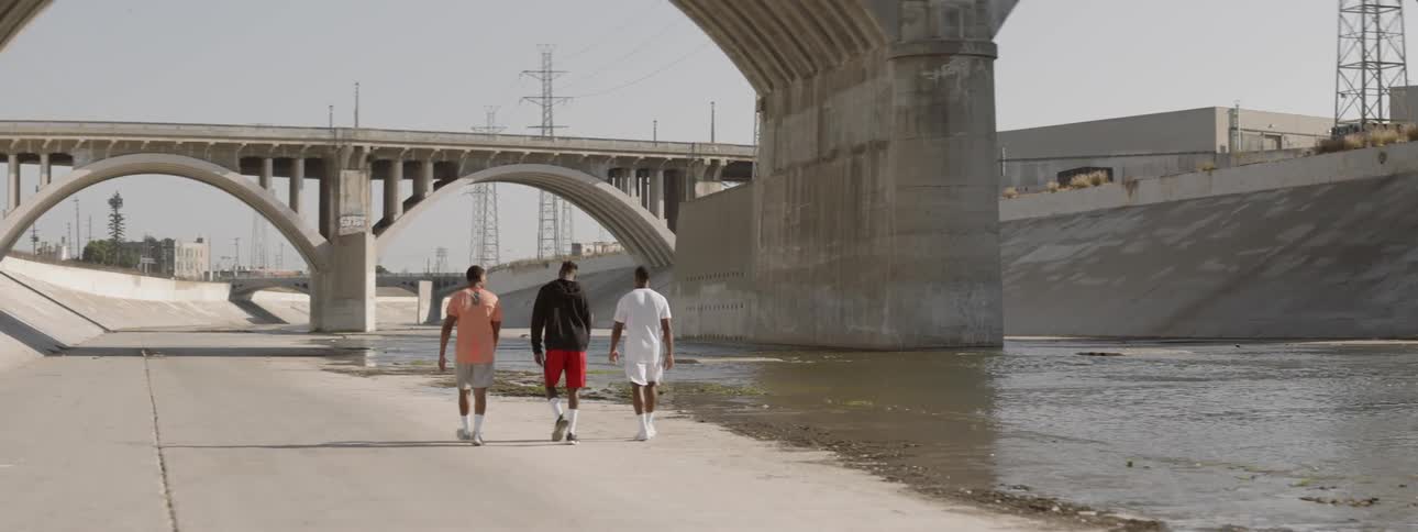 Three men walk along the water in the viaduct on a sunny day