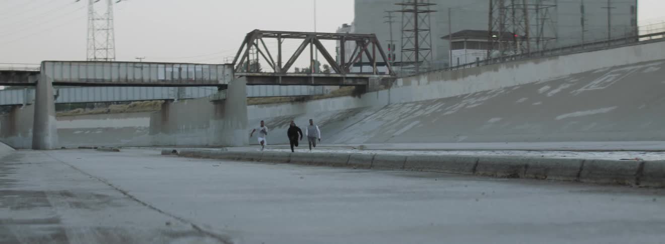 Three men race through a culvert in an industrial area