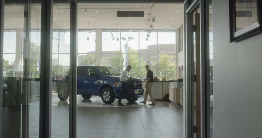 Two men inspect a blue truck inside a car dealership