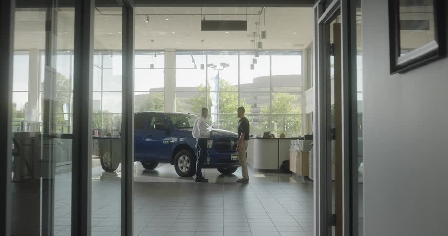 Two men talk about a blue truck inside a dealership showroom
