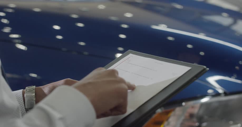 A salesman holding a clipboard makes his pitch in a car dealership