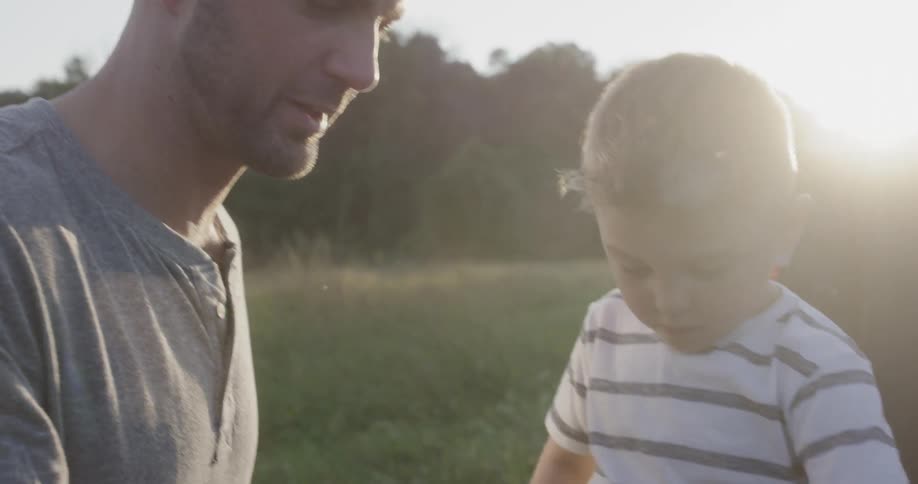 Father and sons talking on the back of a truck in a field at sunset