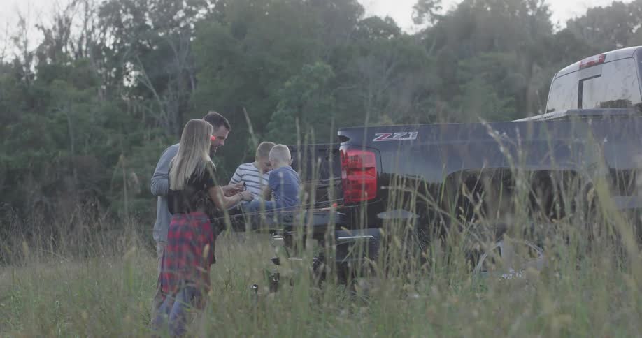 A mother and father play with their two sons who are sitting in the back of a black truck