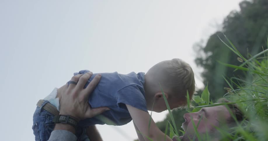 A man laying in a field lifting a small boy