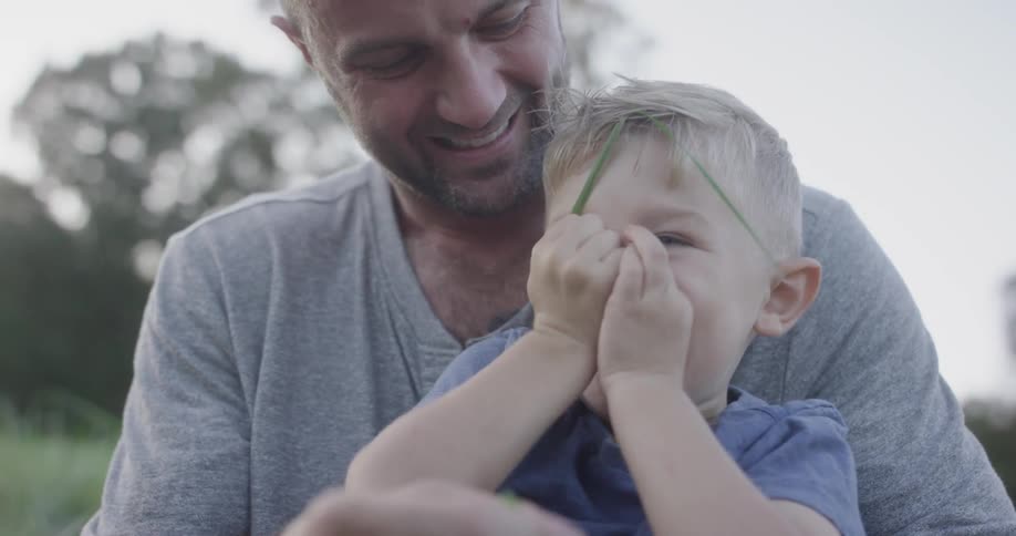 A child plays with a strand of grass while sitting in his fathers lap
