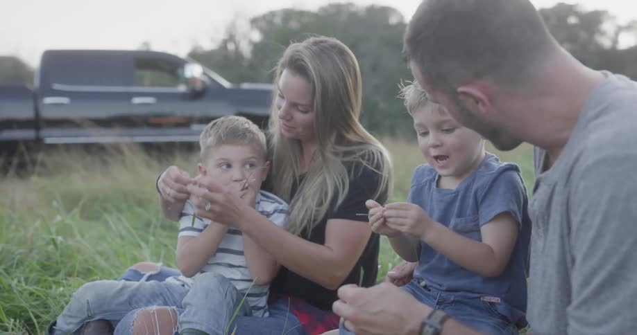 A family sits in a field playing with grass