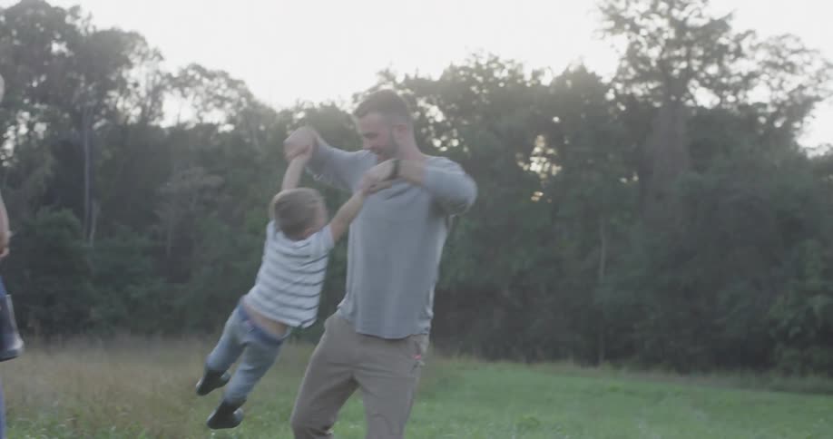 Man hold boys hands and lift up him while woman holds another boy in the forest by day