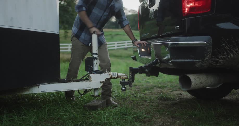 A man turns a trailer hitch crank handle so he can tow the trailer with his truck
