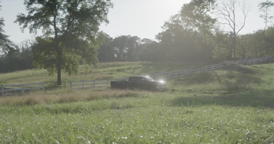 A truck drives through an open gate onto a grassy field