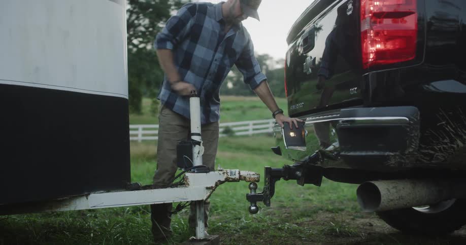 Man turns a crank on a trailer hitch between a truck and a trailer