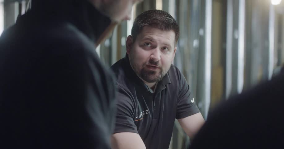 Man talks to the other two men indoors by day