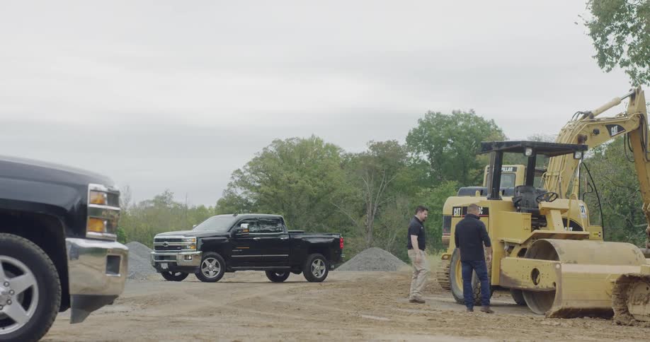 Construction workers are locking up a steamroller as another worker drives up in a pickup truck