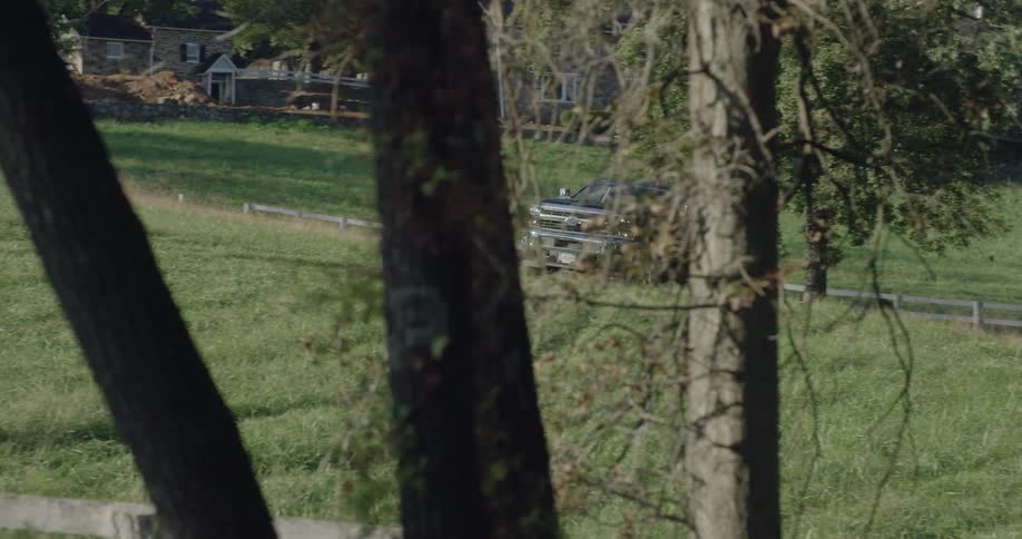 A dark pickup truck drives through a gate and up a grassy slope