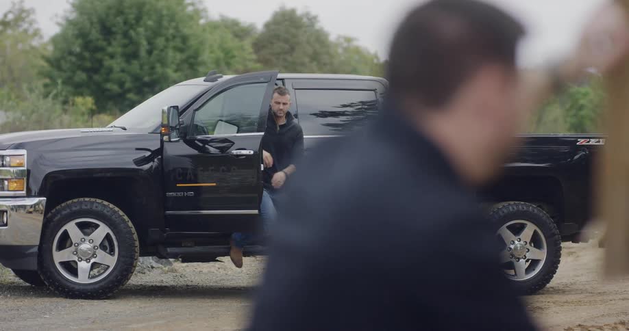 Man getting out of a black truck parked on a dirt road in the country