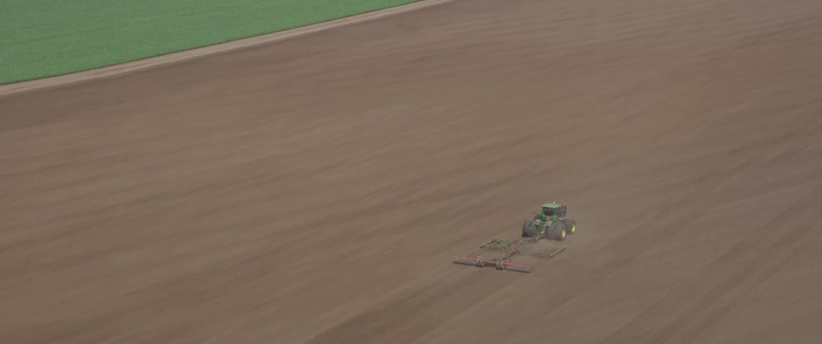 A green tractor pulls a plow in a large dirt field on a farm