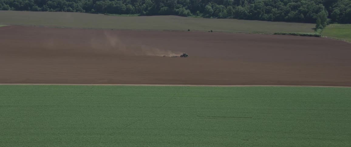 A tractor drives through a dirt field surrounded by vast amount of land
