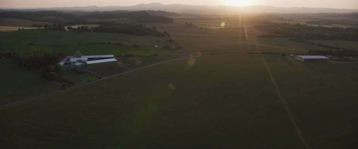 The camera flies over farmland with the sun in the background