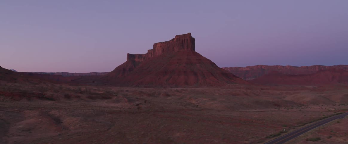The camera flies over a desert landscape looking towards a butte