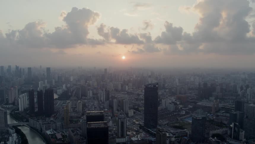 Camera flies over a downtown straight to the setting sun