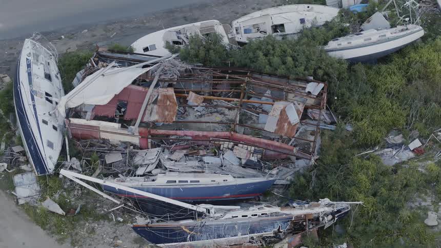 Destroyed sailboats and racing boats are gathered in a pile on the side of the road