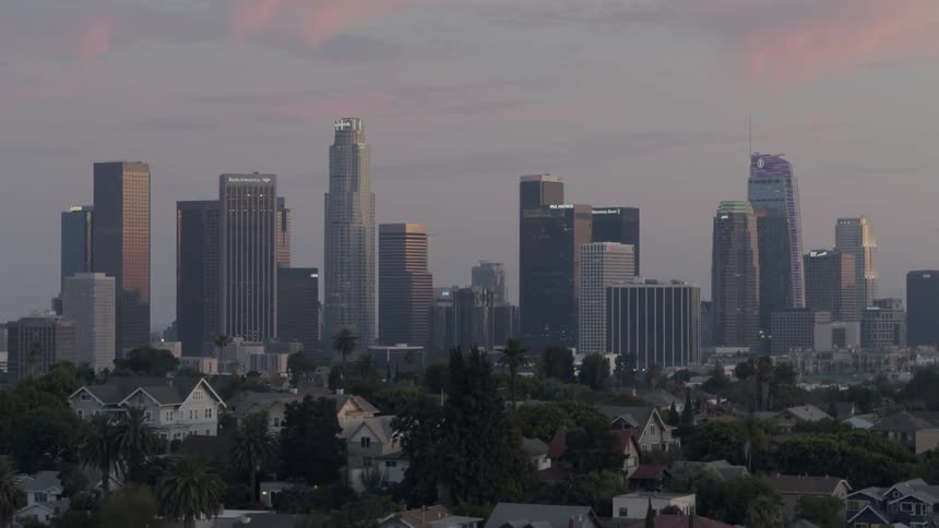 A neighborhood sits in front of a city skyline at dusk