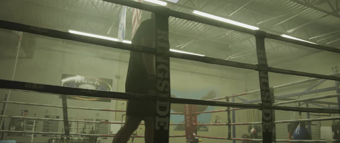 A fighter walking the inside of a boxing ring inside of a gym