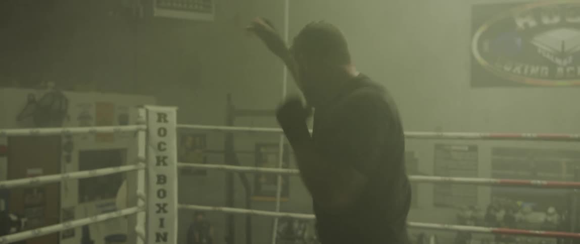 A man shadow boxes in a dimly lit boxing ring
