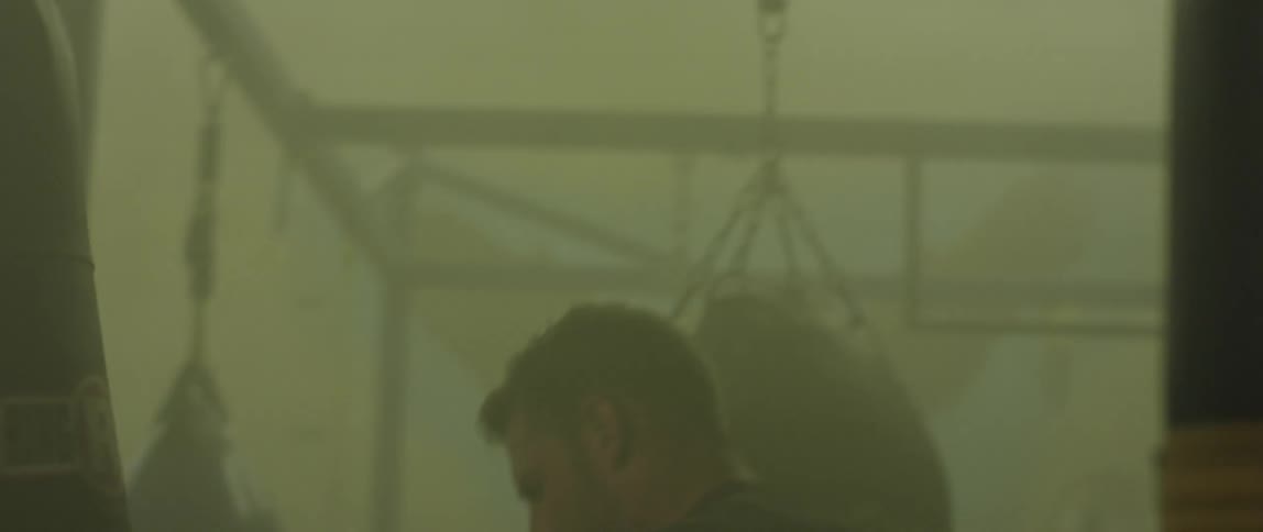 Man punches heavy bag in dimly lit gymnasium