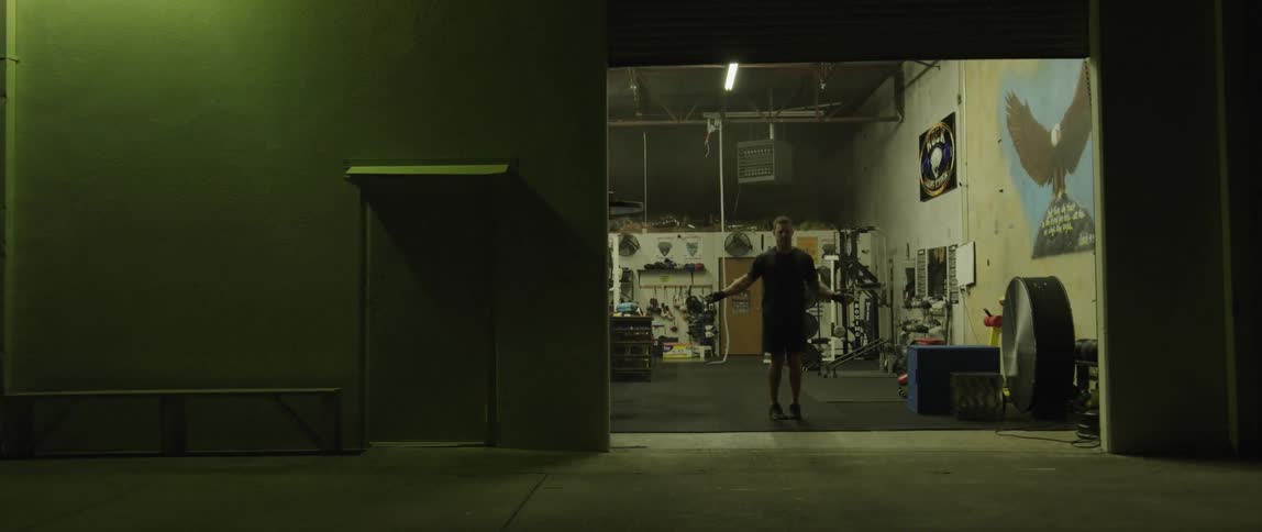 A man jumping rope at the entrance of a gym at night