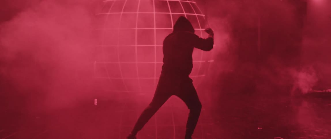 Man wearing hoodie shadow boxes on stage among light show and fog