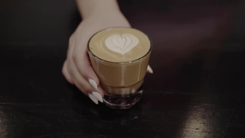 Woman passes a glass of coffee with heart shape indoors
