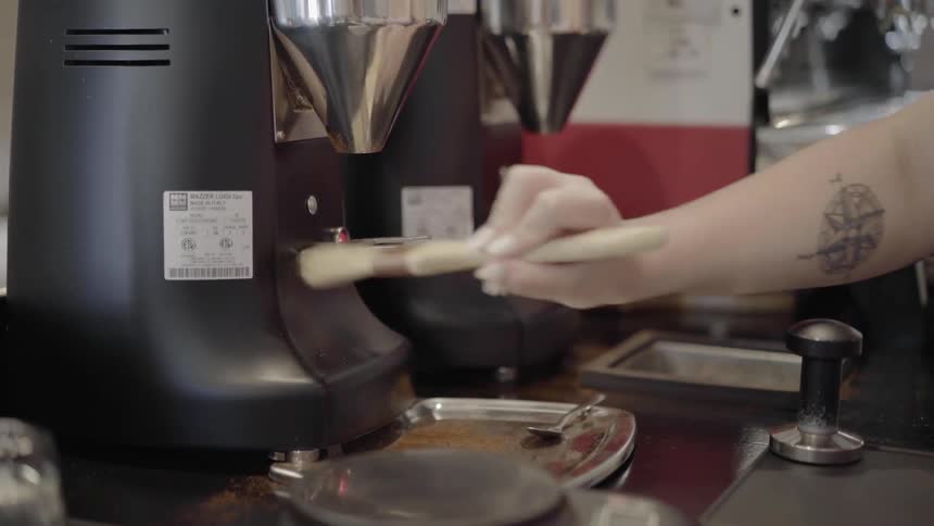 A person dusts off the coffee grinder with a paint brush