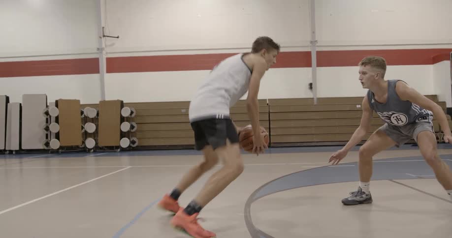 Two boys playing one on one basketball in an indoor court