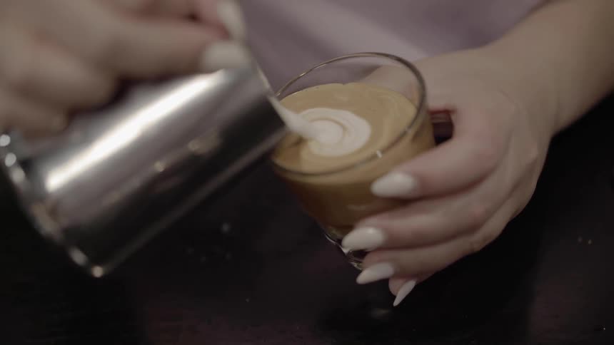 A woman pours cream making a heart shape in a coffee