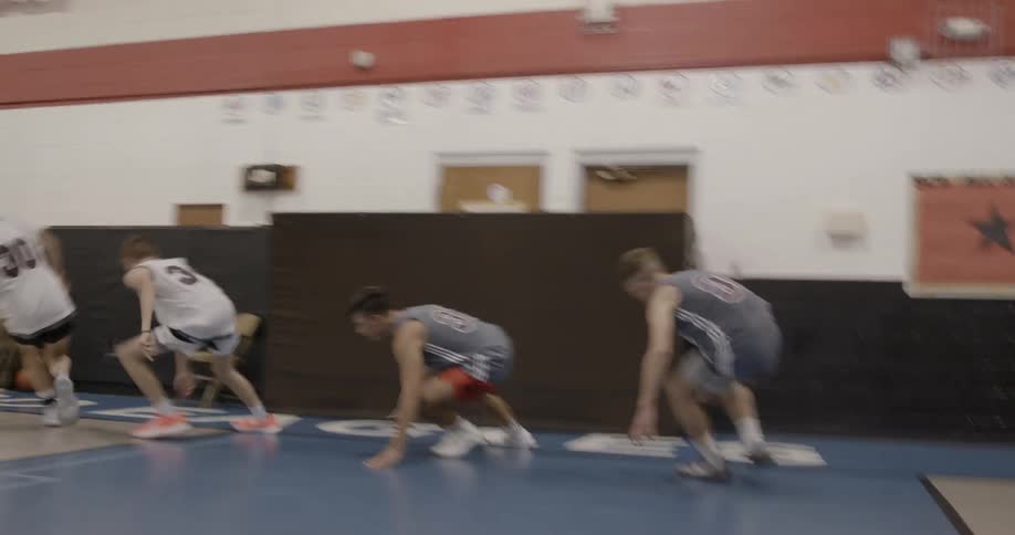 A team oh high school aged boys are in gymnasium and are conducting running drills on a basketball court as their coaches standby and watch in the background