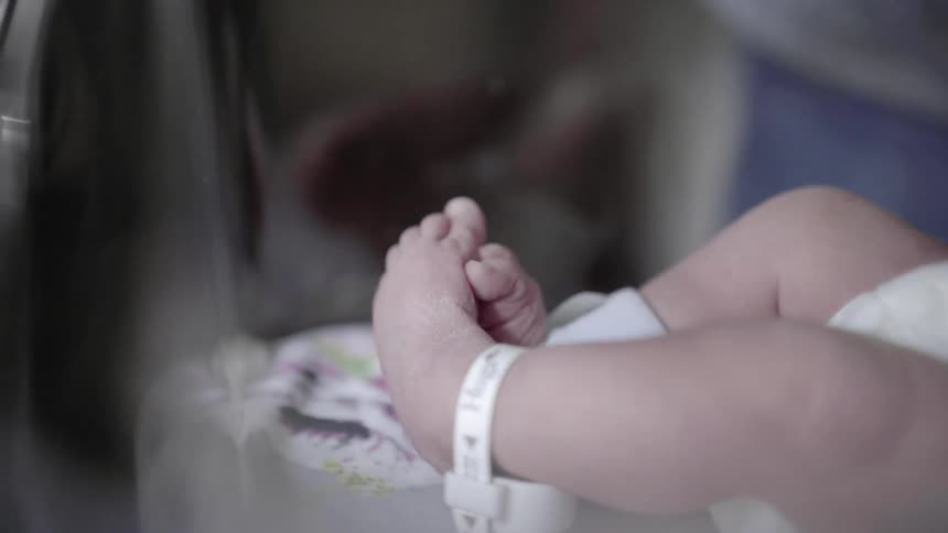 A newborn in a hospital crib wearing an anklet