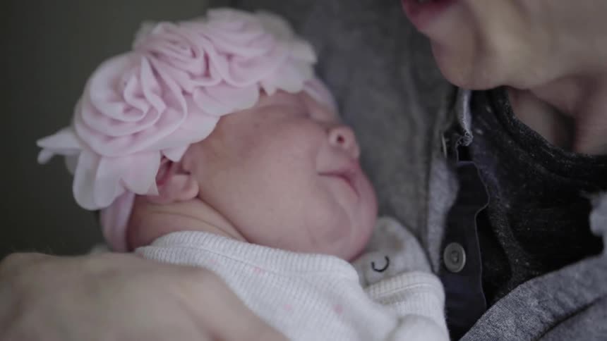 A woman holds a baby who is wearing a pink flower cap