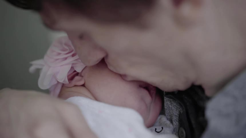 A dad bends his head and kisses his sleeping infant daughter cradled in his arms
