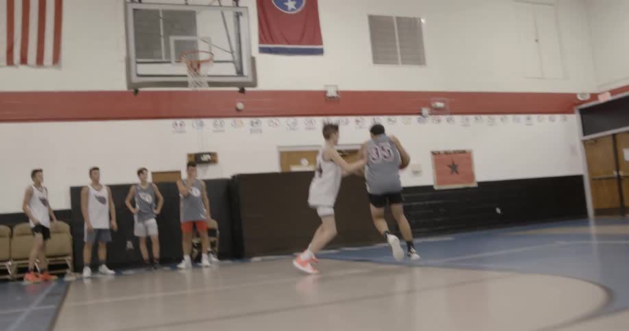 A basketball player runs to the board for a lay up while shoving another player out of the way