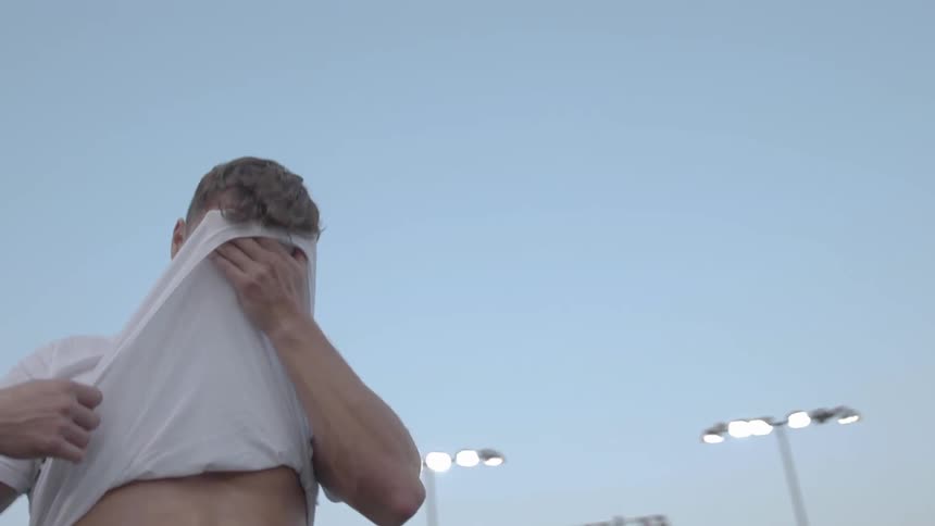 A man wipes his sweaty face with the bottom of his white tee shirt showing his abs