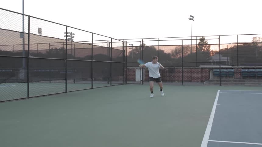 A young man plays tennis at dusk