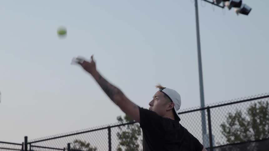 Asian man serves tennis ball in a tennis court