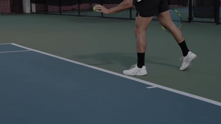 Man bounces tennis ball on court while holding tennis racket