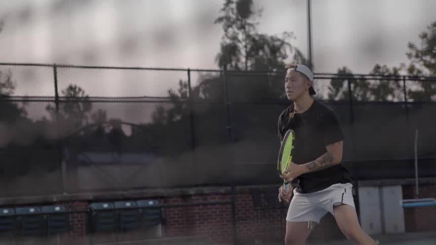 Asian man wearing cap plays tennis on the tennis court at dusk