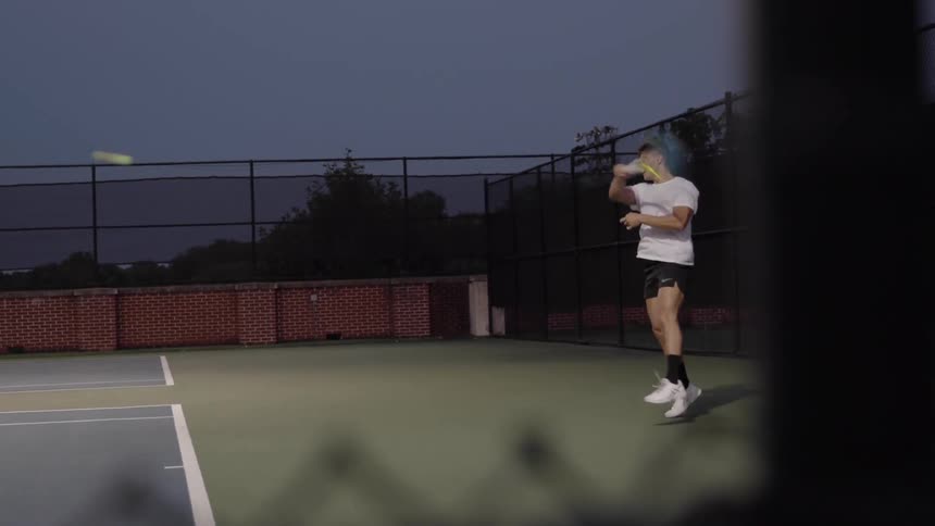 A man playing tennis on a court at night