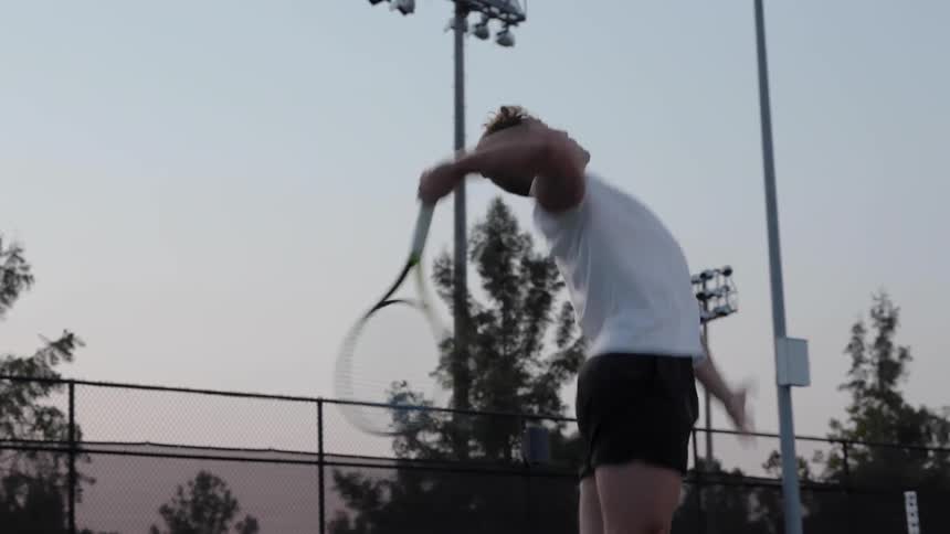 A man throws a tennis ball and leaps to hit it