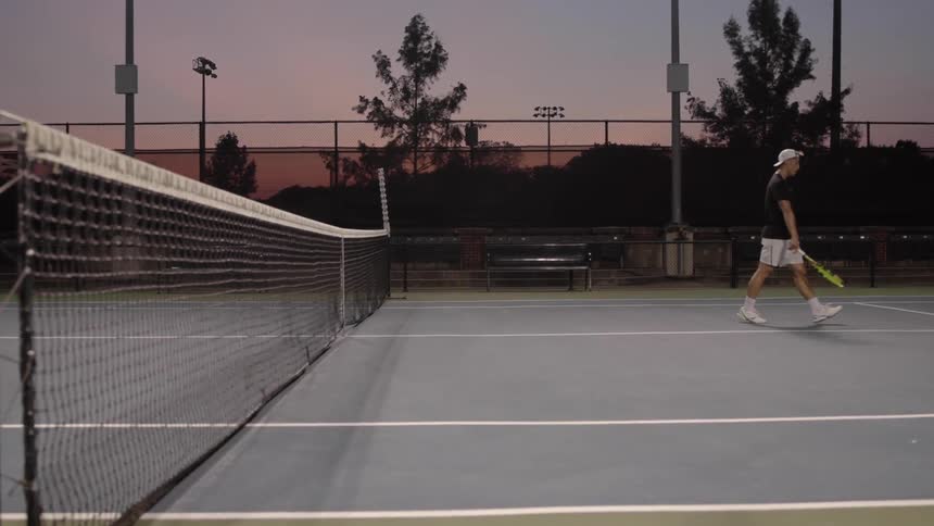 Man dribbles tennis ball and walks toward end of court