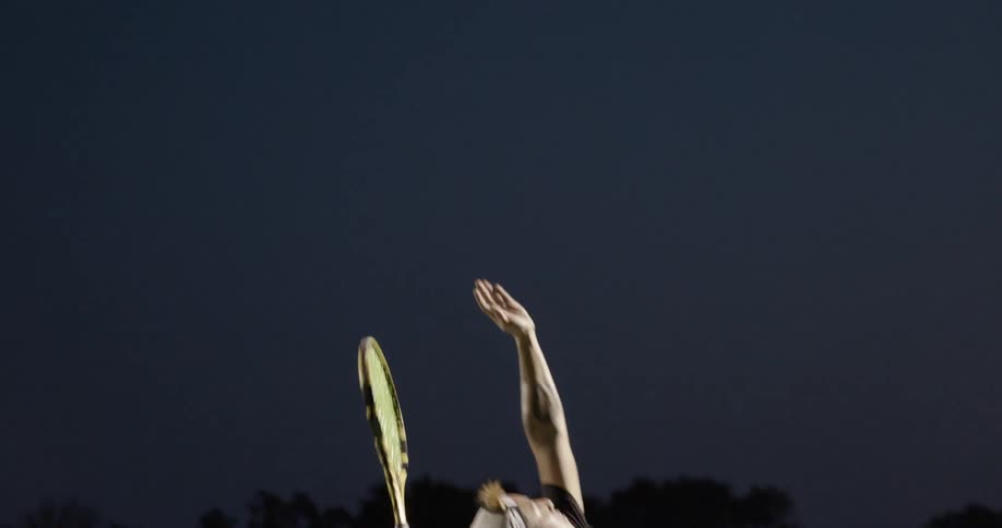 Two men play tennis on a tennis court at night