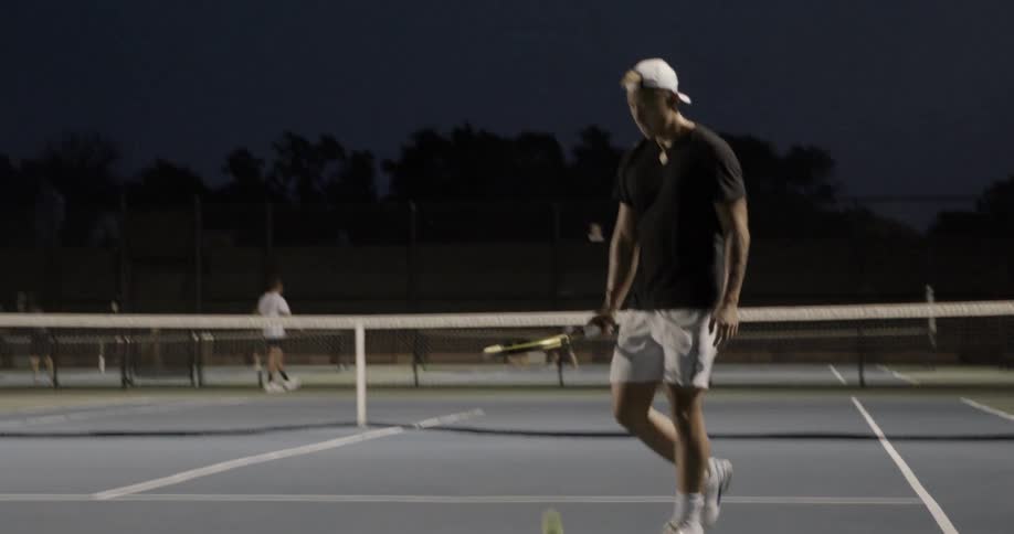 A white male tennis player dribbling a tennis ball with his tennis racquet