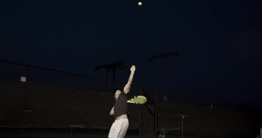 Man serves tennis ball at night